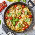 Pesto chicken breasts in a skillet with cherry tomatoes, fresh basil leaves, and garlic in a savory sauce