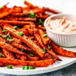 Crispy air fryer carrot fries on a white plate with fresh herbs and dipping sauce