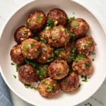 Golden brown air fryer meatballs garnished with chopped parsley in a white bowl on a marble surface