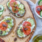 Low carb avocado bread topped with cucumbers, tomatoes, and creamy spreads on a wooden board