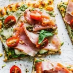 Low carb pesto chicken crust pizza slices topped with cherry tomatoes, ham, mozzarella, and fresh basil